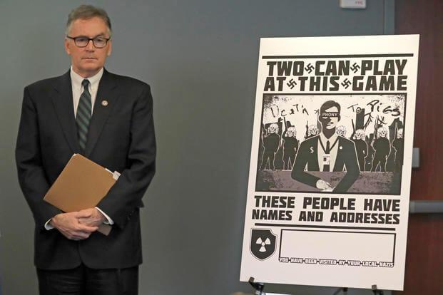 U.S. Attorney Brian Moran stands next to a poster that was mailed to the home of Chris Ingalls, an investigative reporter with KING-TV in Seattle, Wednesday, Feb. 26, 2020, during a news conference in Seattle. (AP Photo/Ted S. Warren) U.S. Attorney Brian Moran stands next to a poster that was mailed to the home of Chris Ingalls