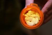 Fingers hold an open pill bottle against a black background.