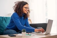 A woman sits on a couch while working on a computer.