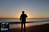 A man in a WWII uniform stands on Omaha Beach